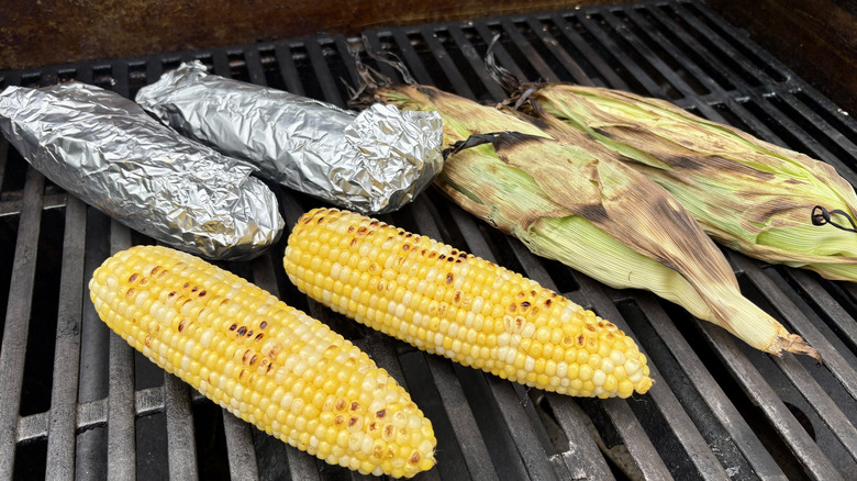 Six ears of corn on a grill, two in husks and two in foil
