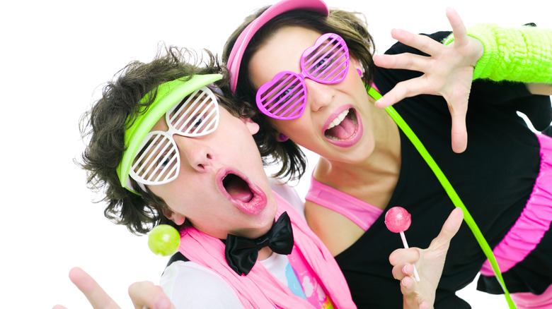 Teens wearing 1980s fashions with neon lollipops in hand