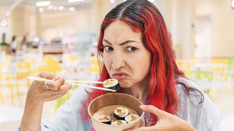 Woman with crinkled up nose from odor while eating sushi