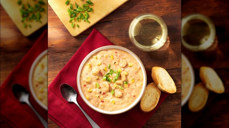 bowl of chowder with red napkin, spoon, sliced bread, white wine