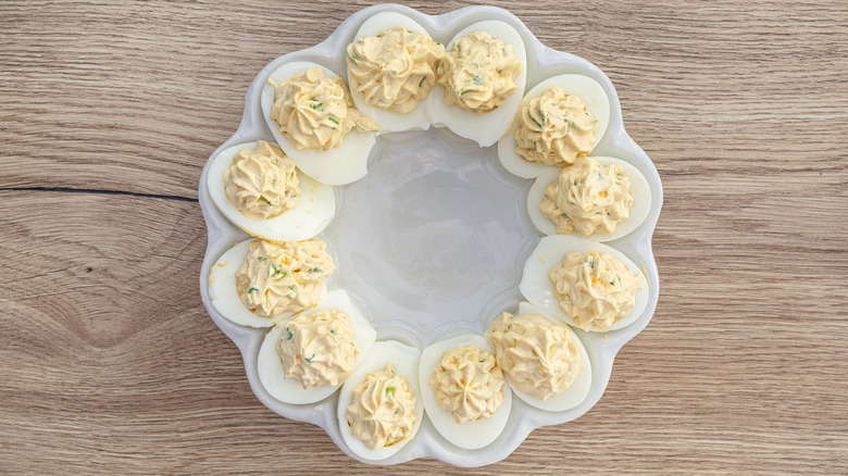 Classic deviled eggs on a white plate with wooden background