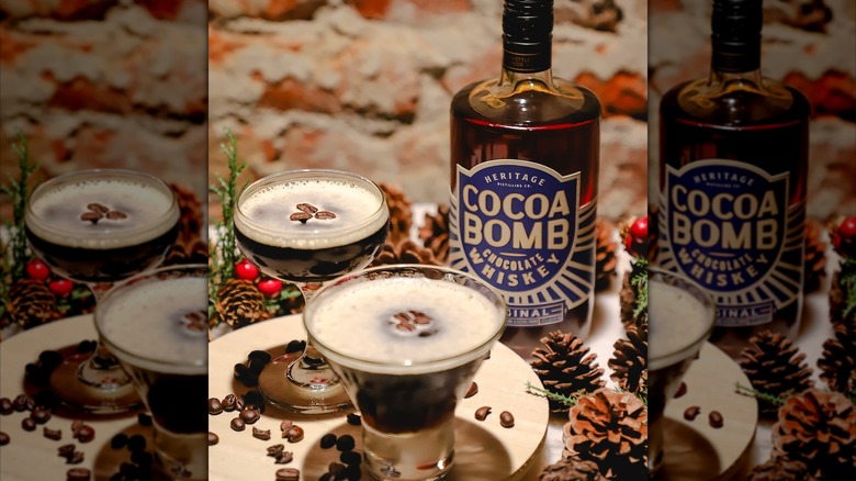 Bottle of Heritage Cocoa Bomb Chocolate Whiskey with two espresso martinis with pinecones and espresso beans sprinkled around