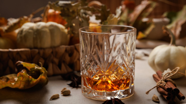 Glass of whiskey with leaves and fall seasonings and aspices