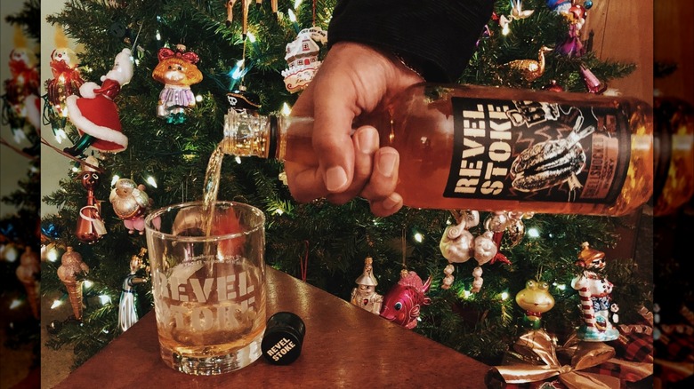 Pouring Revel Stoke Shellshocked Roasted Pecan whisky into a glass with Christmas tree in the background