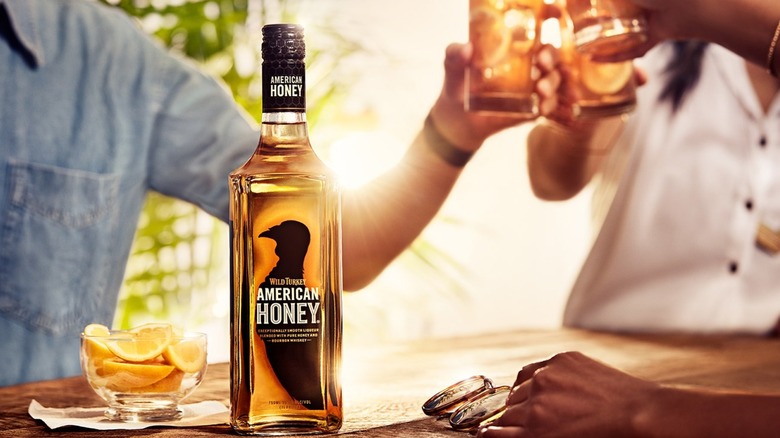 People clinking glasses with bottle of Wild Turkey American Honey in the front with bowl of lemon slices
