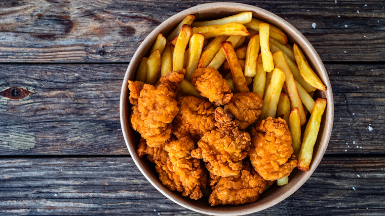 Aerial photo of a bowl of chicken nuggets and french fries in a container on a wooden table