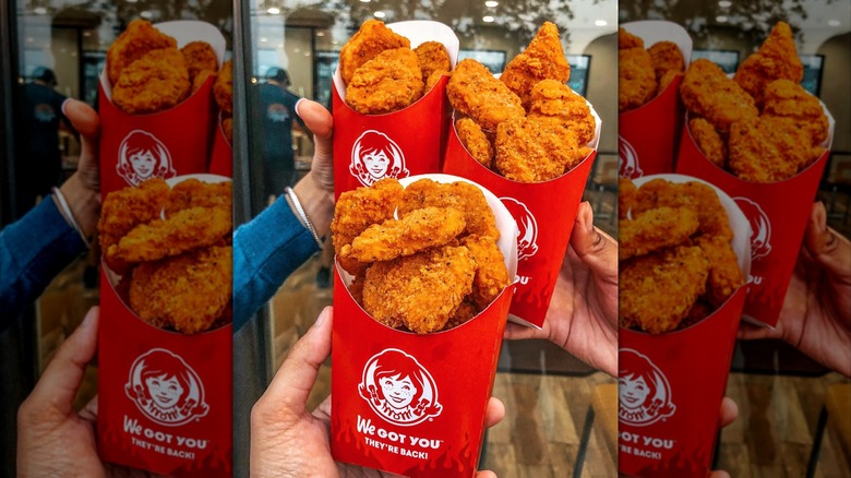Three hands holding up containers of Wendy's spicy chicken nuggets