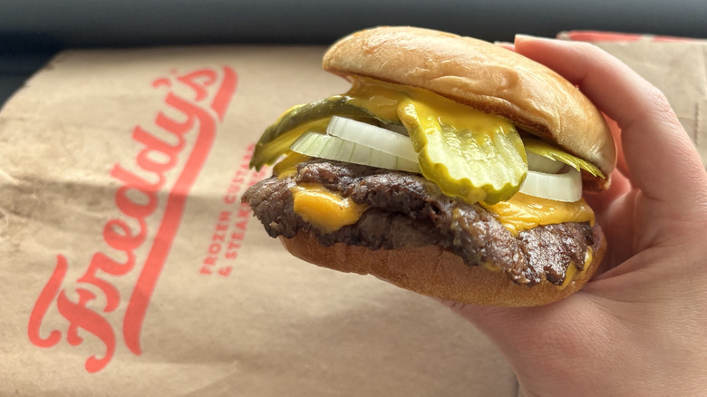 Hands holding Freddy's smash patties with American cheese and large pickle slices