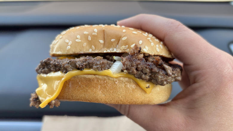 Hand holding a McDonald's quarter pounder with cheese in sesame seed bun
