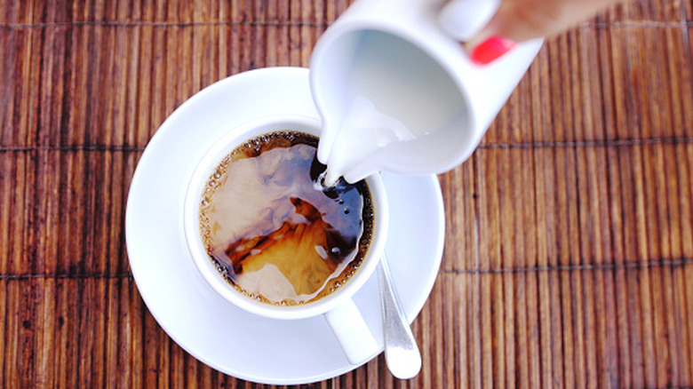 Hand pouring creamer into a cup of black coffee