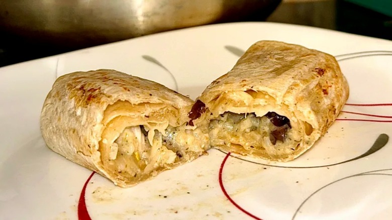A Red's All Natural frozen burrito that has been reheated and cut in half on a decorative white plate with a red swirl design