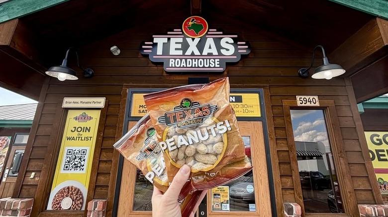 Hand hold two bags of Texas Roadhouse peanuts in front of the restaurant entrance