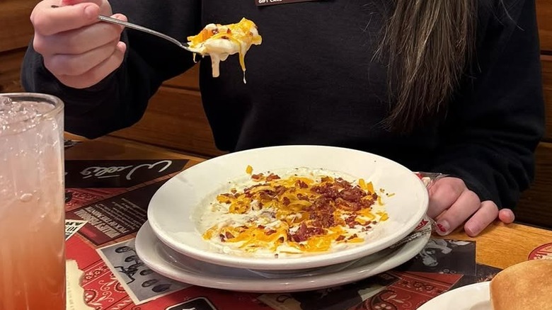 Person eating Texas Roadhouse baked potato soup in a white bowl