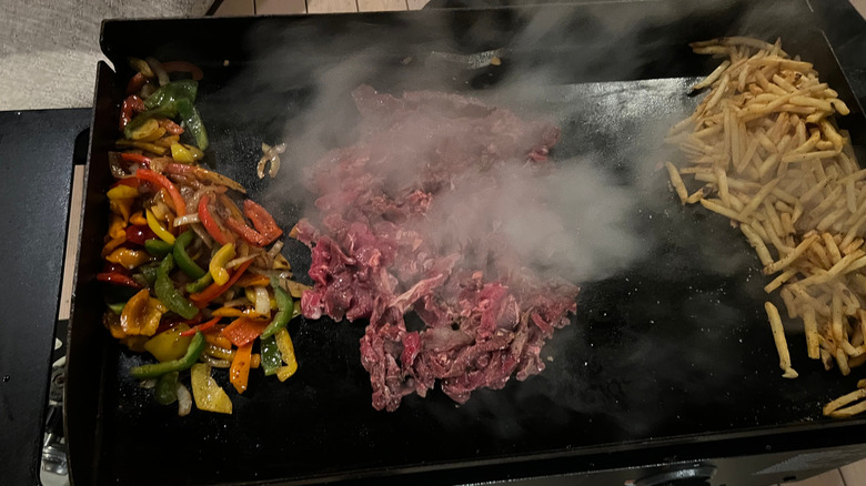 Top view of a flat top with peppers, steak, and fries