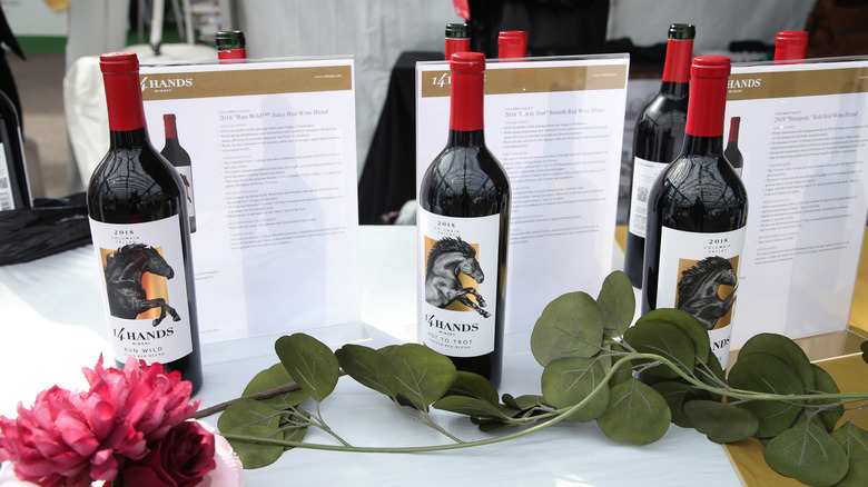 Three bottles of 14 Hands wine with info sheets behind and decorative greenery and flowers in front