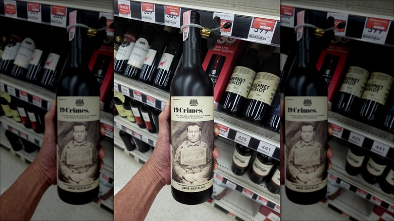 A hand holding a bottle of 19 Crimes wine in the wine aisle of a store