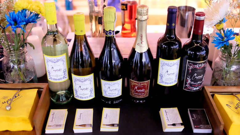 Six different bottles of Cupcake Vineyards wine lined up on black tablecloth surrounded by flowers in jars