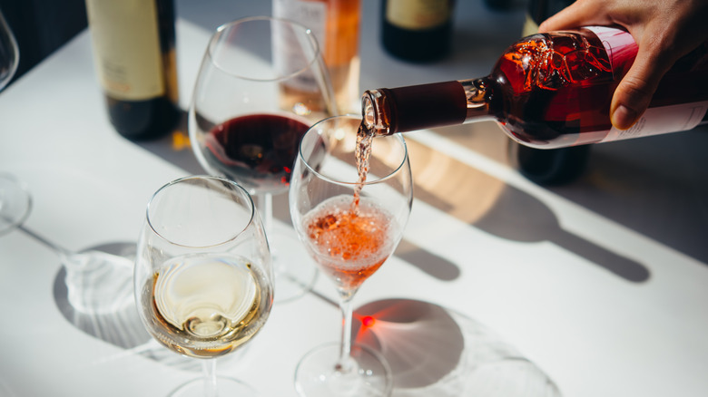 A glass of white wine and red wine with a bottle of wine pouring rosé into another glass