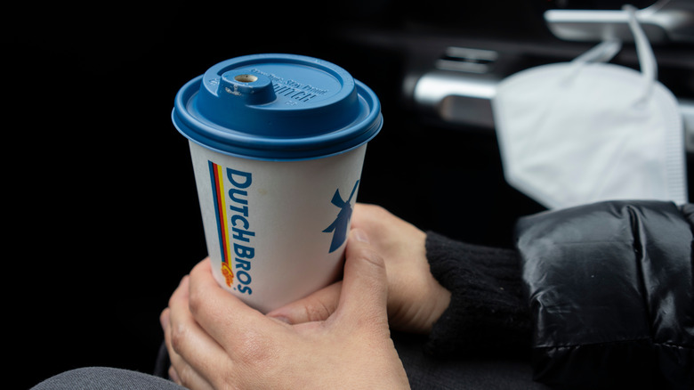 Dutch Bros paper coffee cup in mans hands in car