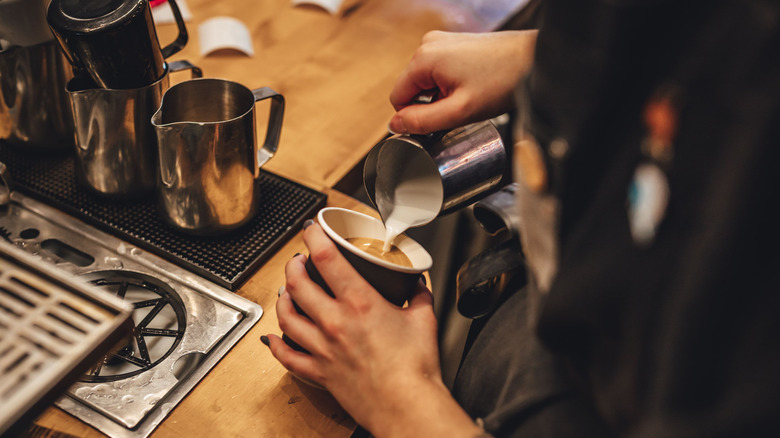barista adding foamed milk to coffee on crowded countertop at coffee shop