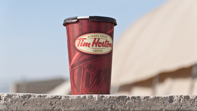 Tim Hortons paper coffee cup with lid on concrete ledge outdoors