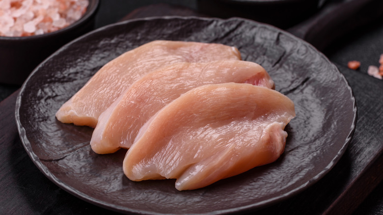 Three raw, boneless chicken breast fillets on a dark ceramic plate
