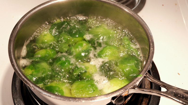 A close-up of Brussels sprouts boiling in a stainless-steel pot on a stovetop
