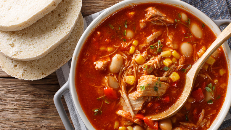 A pot of Brunswick stew on a wooden table next to sliced bread