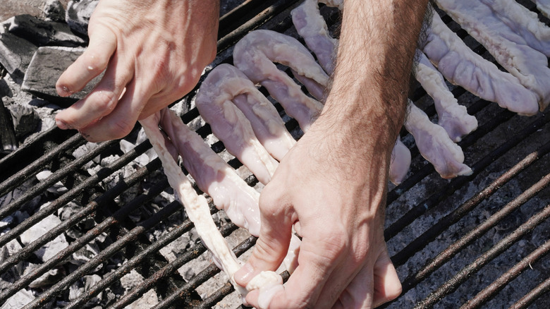 Close-up of a man's hands setting raw chitlins on a grill