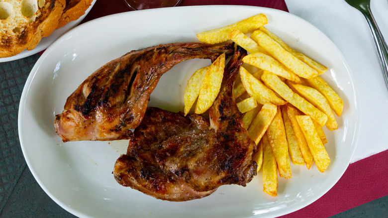 Fried rabbit served with French fries on a white plate