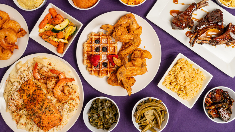 A spread of soul food including chicken and waffles, collard greens, and fried shrimp