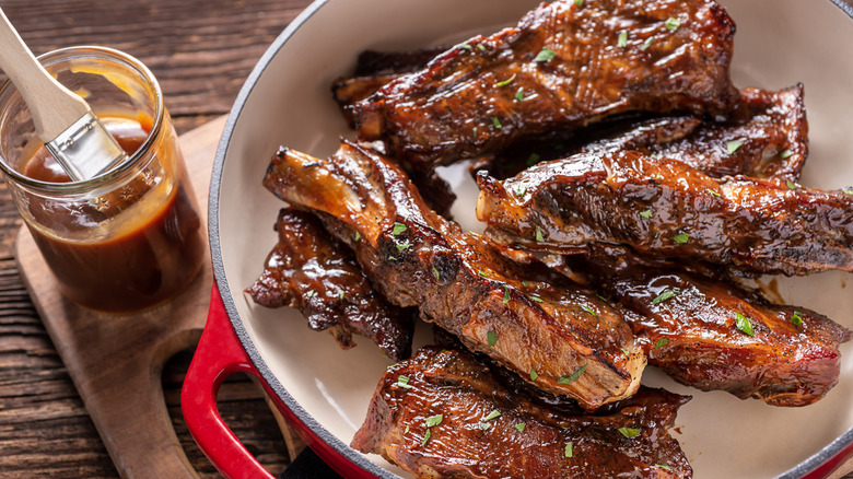 jar of barbecue sauce with brush beside plate of barbecue ribs