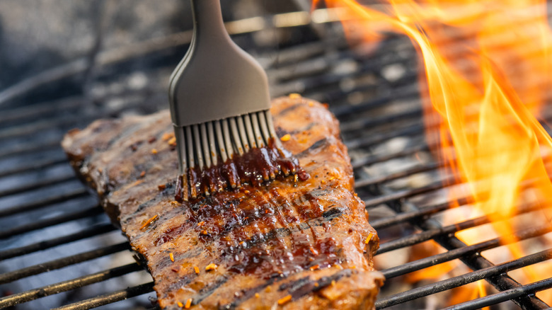 Ribs brushed with barbecue sauce over flame on grill