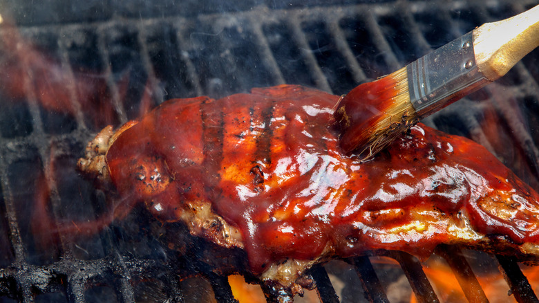chicken breast being brushed with sauce over flames on grill
