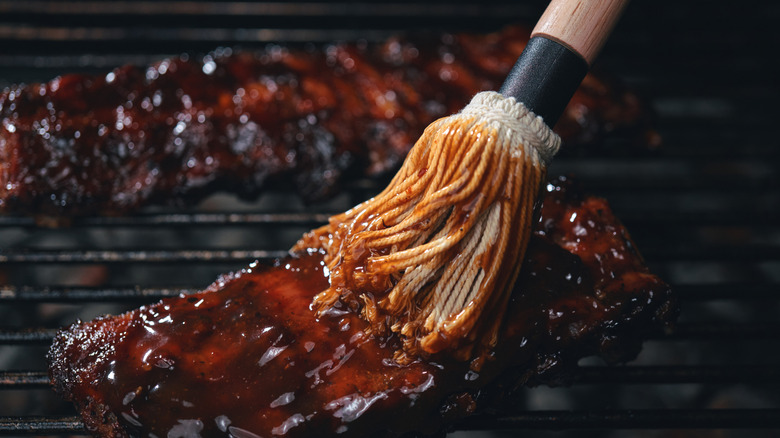 mop brush applying sauce to ribs on grill grates