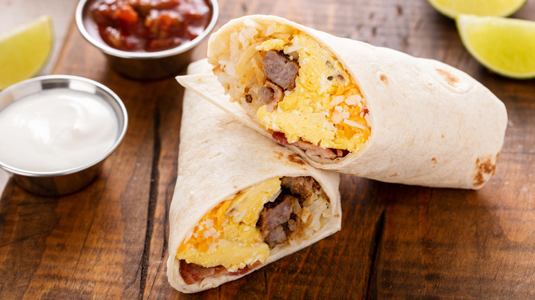 Breakfast burrito halves filled with eggs and sausage on cutting board