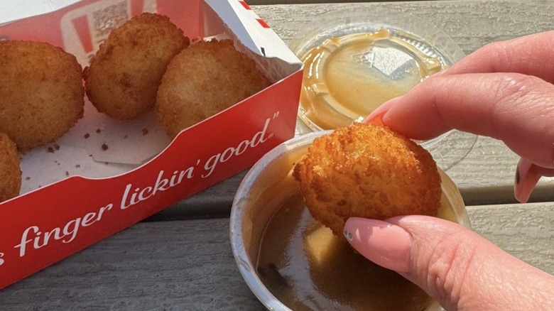 Hand dipping KFC Mashed Potato Poppers into a plastic to-go cup of gravy