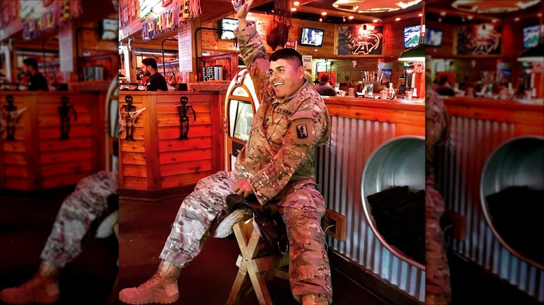 A man in a military uniform playfully sitting on the Texas Roadhouse birthday saddle