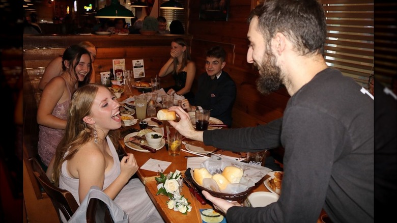 A young woman smiling while being hand-fed a roll by a Texas Roadhouse waiter
