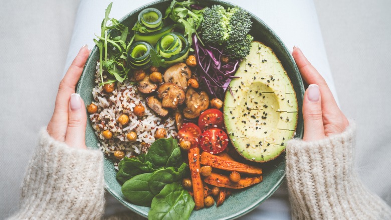 hands hold plate with healthy foods spinach avocado mushrroms tomatoes