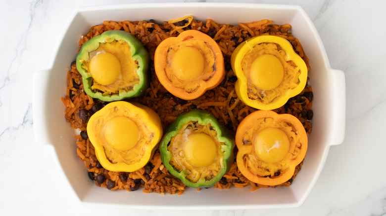 bell peppers with raw eggs in a white baking pan