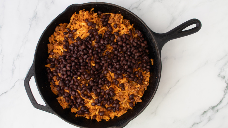 black beans, shredded potatoes, and ground meat in black frying pan