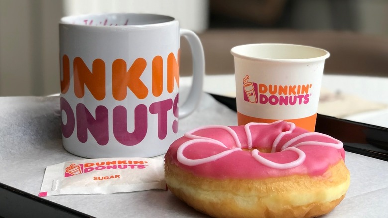White Dunkin' mug next to paper cup and donut