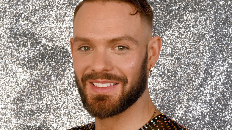 John Whaite smiling in front of silver background