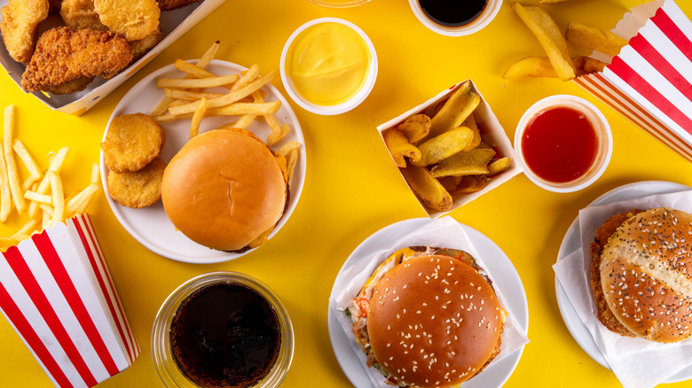 Fast food burgers, fries, chicken nuggets, drinks, and sauces on yellow background