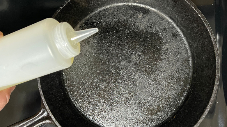 Squeeze bottle of oil hovering above cast iron skillet