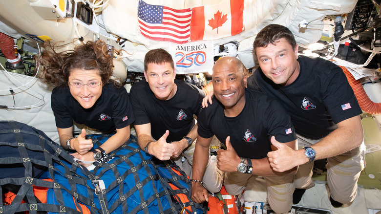 Crew of the Artemis II in space with a banner honoring America's 250th anniversary in the background.