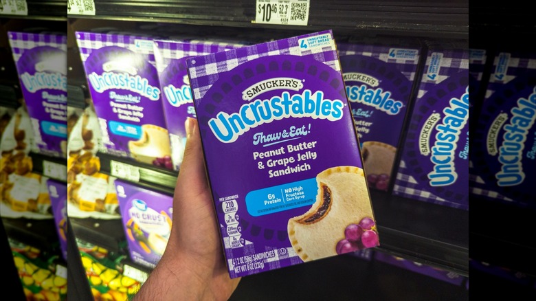 Person holding box of grape Uncrustables inside a grocery store.