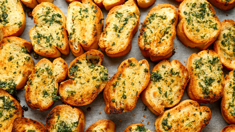 Rows of garlic bread slices topped with chopped fresh herbs