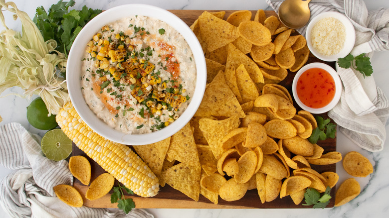 Bang bang corn dip served on board with various chips and fresh ear of corn